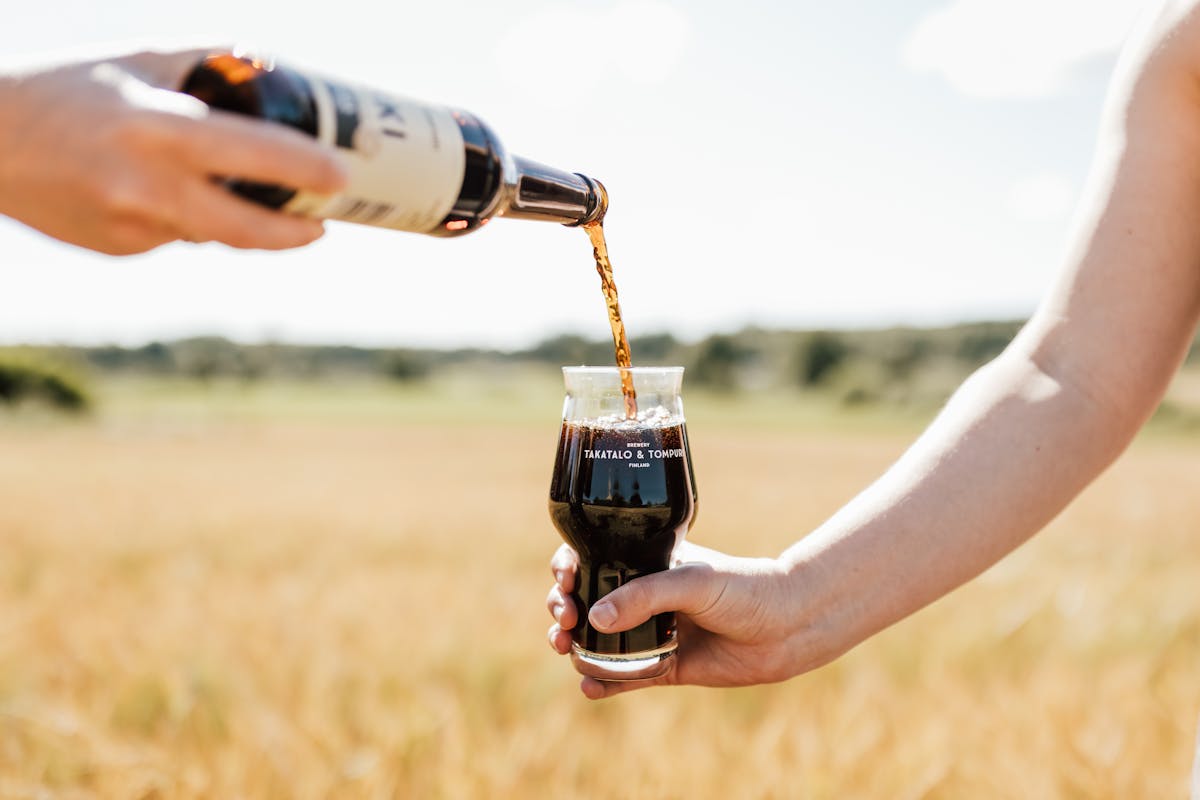 Takatalo ja Tompuri oy:n olutta kaadetaan lasiin pellolla. 