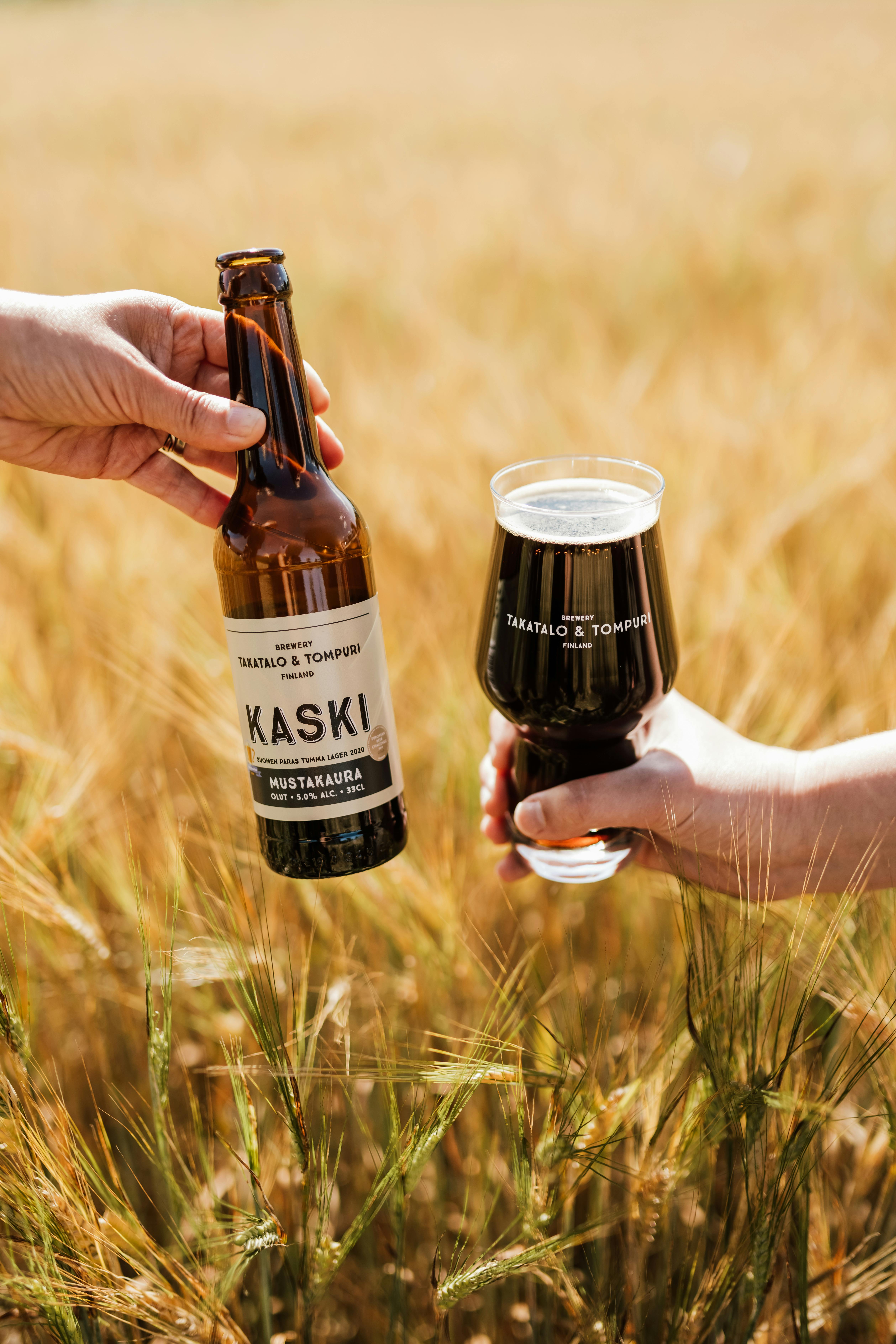 Takatalo ja Tompuri olutpanimon olutpullo ja olutta lasissa pellolla.